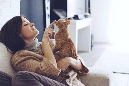 Donna seduta su una poltrona che tiene un gatto rosso tigrato e gli tocca delicatamente il naso
