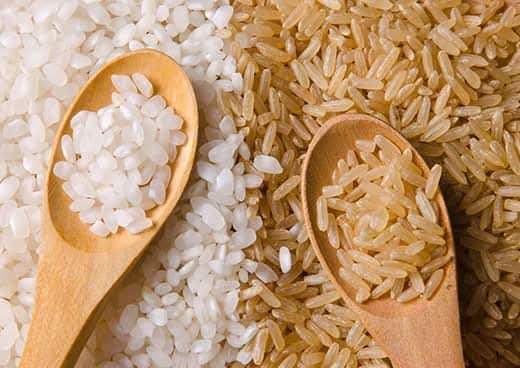 Mucchi di riso bianco e integrale l'uno accanto all'altro, con cucchiai in legno pieni di riso.